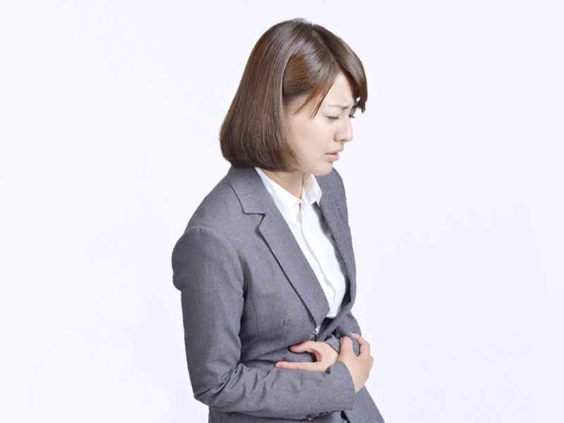 仕事中にお腹をおさえる女性